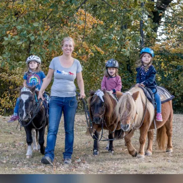 Barbara Greb führt drei Kinder auf Ponys über eine herbstliche Wiese