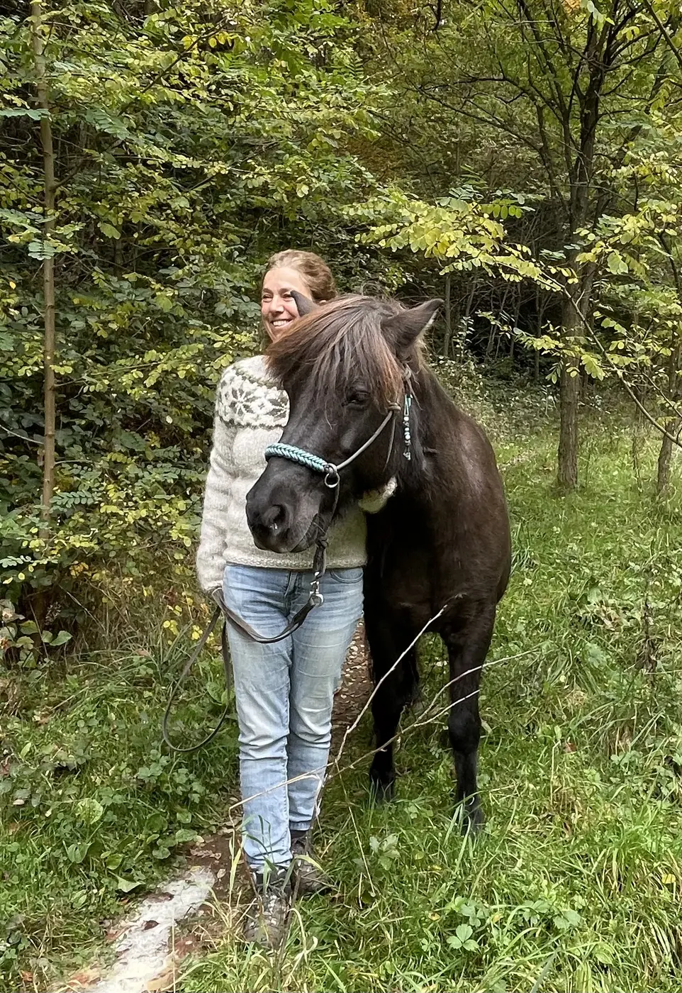 Junge Reiterin mit einem dunklen Islandpferd im Wald
